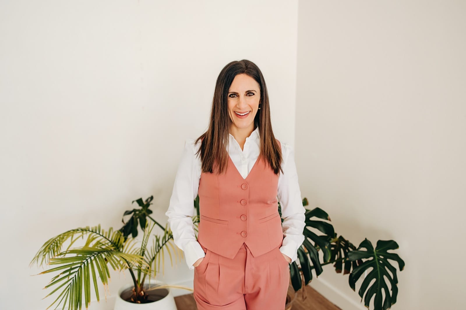 Nicole Runyon smiling in a pink suit, standing between green plants